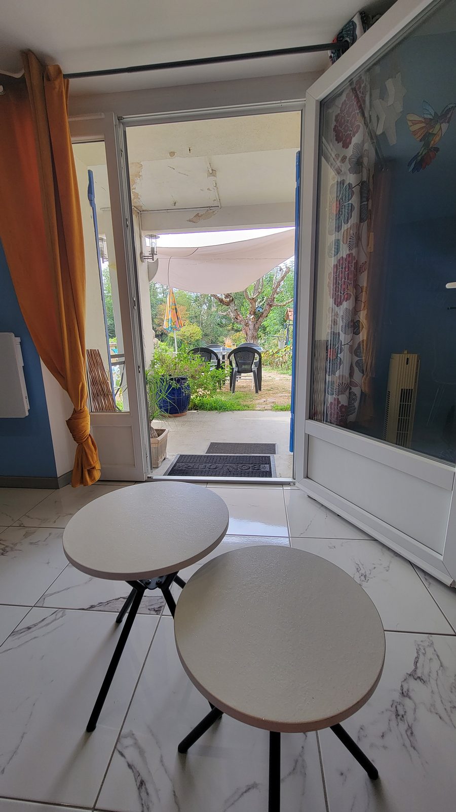 Porte-fenêtre de la pièce de vie ouverte sur la terrasse ombragée et le jardin