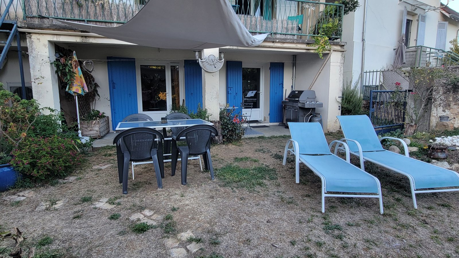 La terrasse ombragée et les volets bleus de l’appartement, vus du jardin